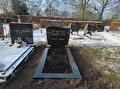 Een besneeuwde begraafplaats met meerdere grafstenen. Vooraan staat een zwarte grafsteen met Arabisch schrift aan het uiteinde van een rechthoekig grafvak met kale aarde.